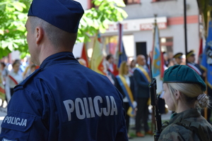 na zdjęciu policjant tyłem do aparatu, obok niego przedstawicielka wojska, przed nimi uczestnicy wydarzenia