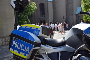 na zdjęciu policyjny motocykl, w oddali miejsce wydarzenia z uczestnikami