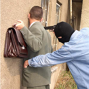 zdjęcie przedstawia mężczyznę opartego twarzą o mur. Za nim stoi zamaskowany mężczyzna i przykłada mu pistolet do pleców