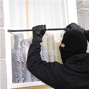zdjęcie przedstawia zamaskowanego mężczyznę, który łomem próbuje podważyć okno