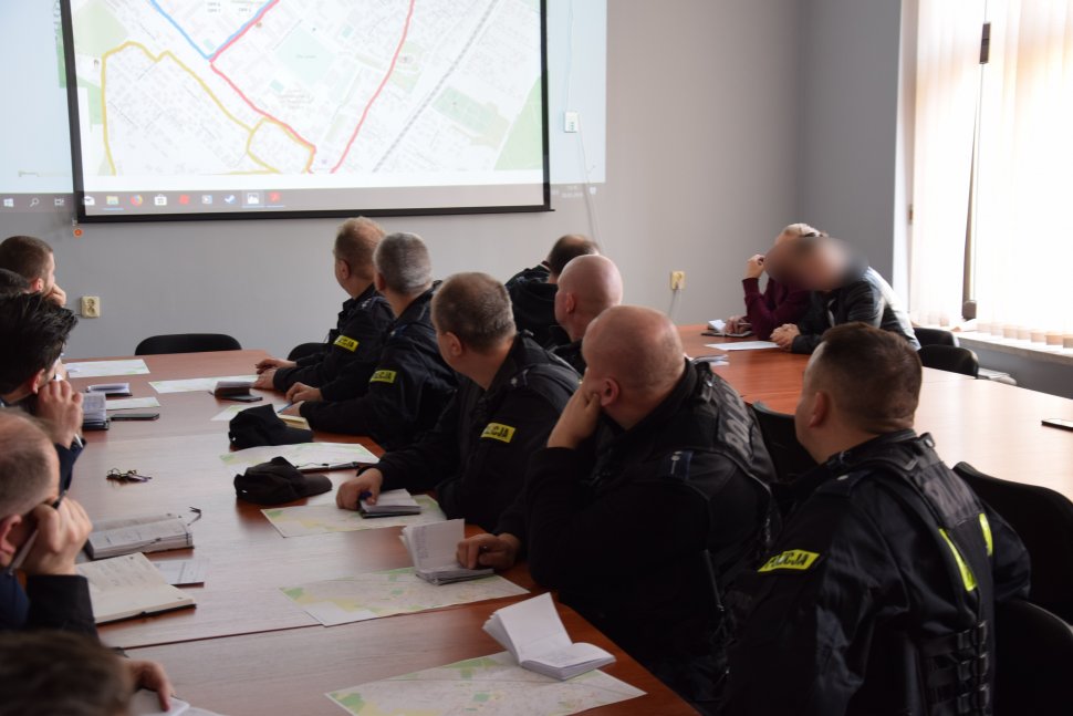 zdjęcie przedstawia salę odpraw, na której, przy stołach siedzą policjanci 
