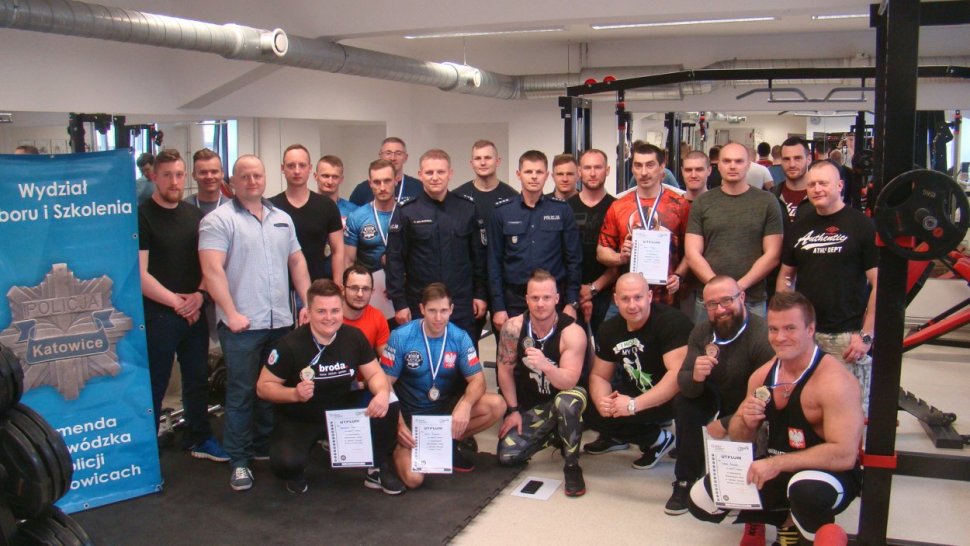 zdjęcie przedstawia salę siłowni, w której grupa sportowców pozuje do zdjęcia