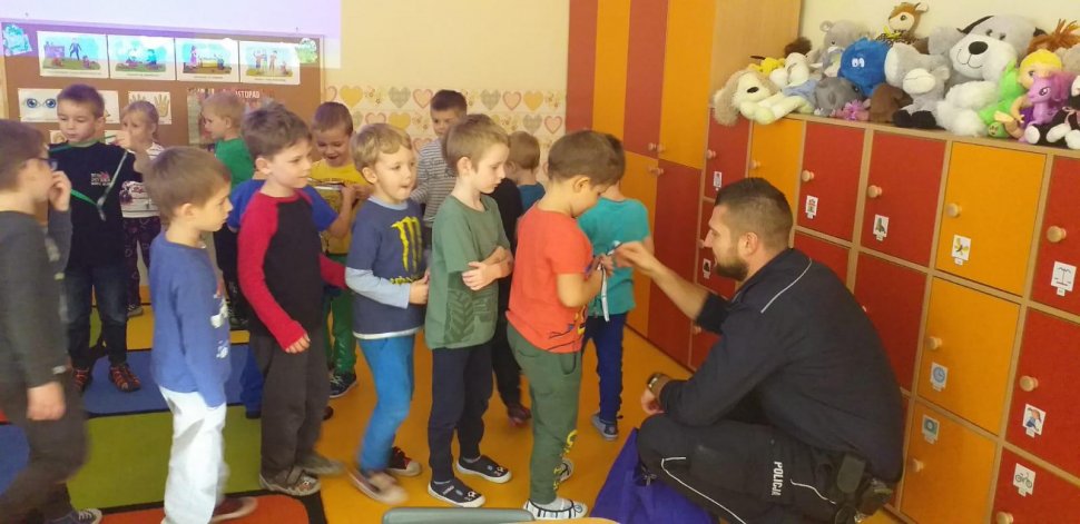 na zdjęciu widać szkolną klasę, w której policjant rozdaje uczniom odblaskowe zawieszki 