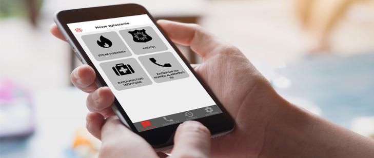 Na fotografii widać dłoń, w której znajduje się telefon komórkowy. Na wyświetlaczu widać aplikację Alarm112