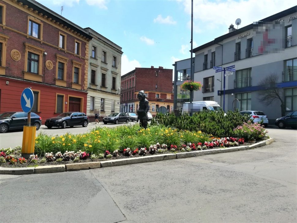 Na fotografii widać zielone rondo, dookoła którego znajdują się budynki i samochody 