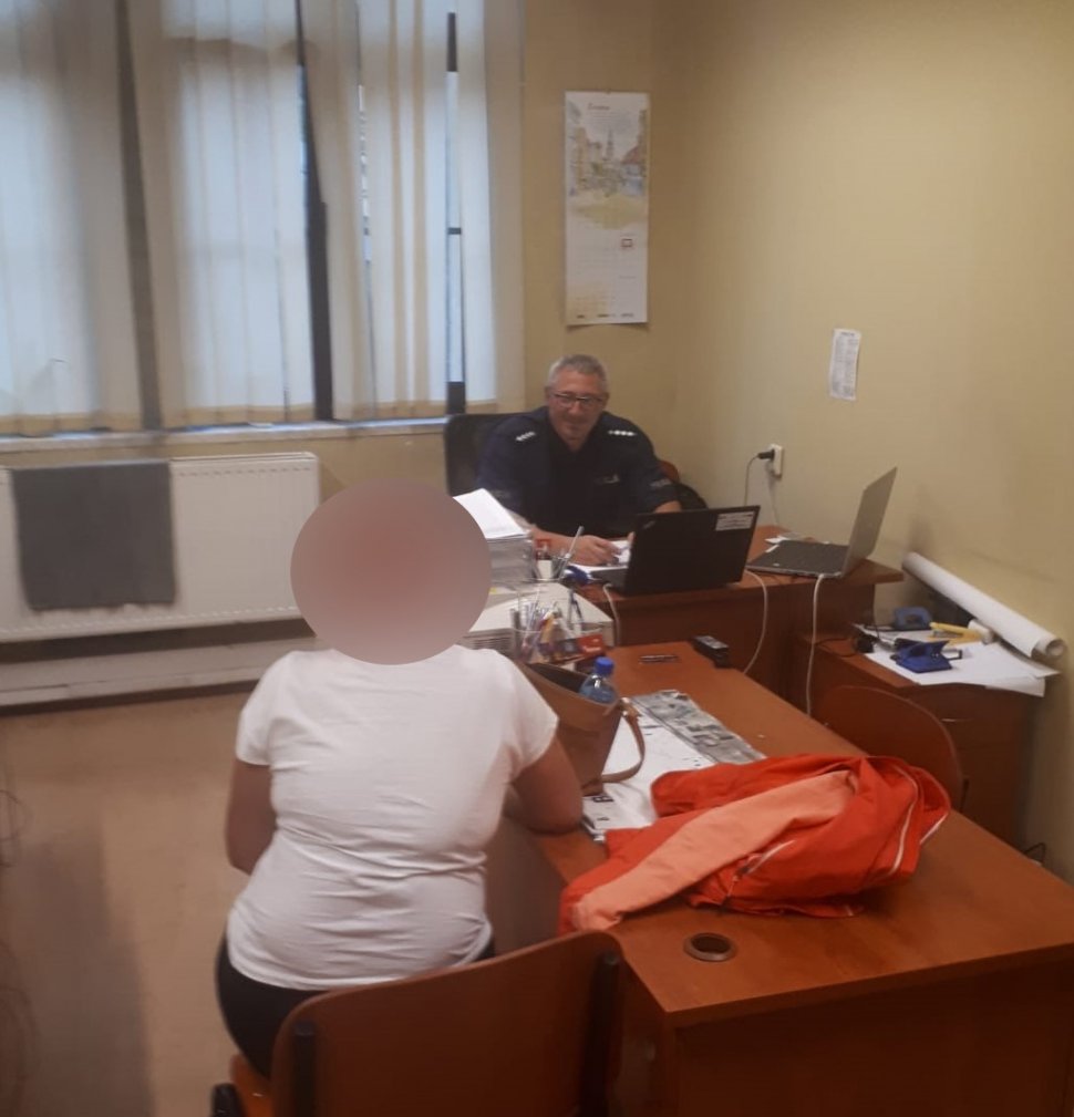 N zdjęciu widać pokój, w którym przy biurku siedzą policjant oraz zatrzymana kobieta 