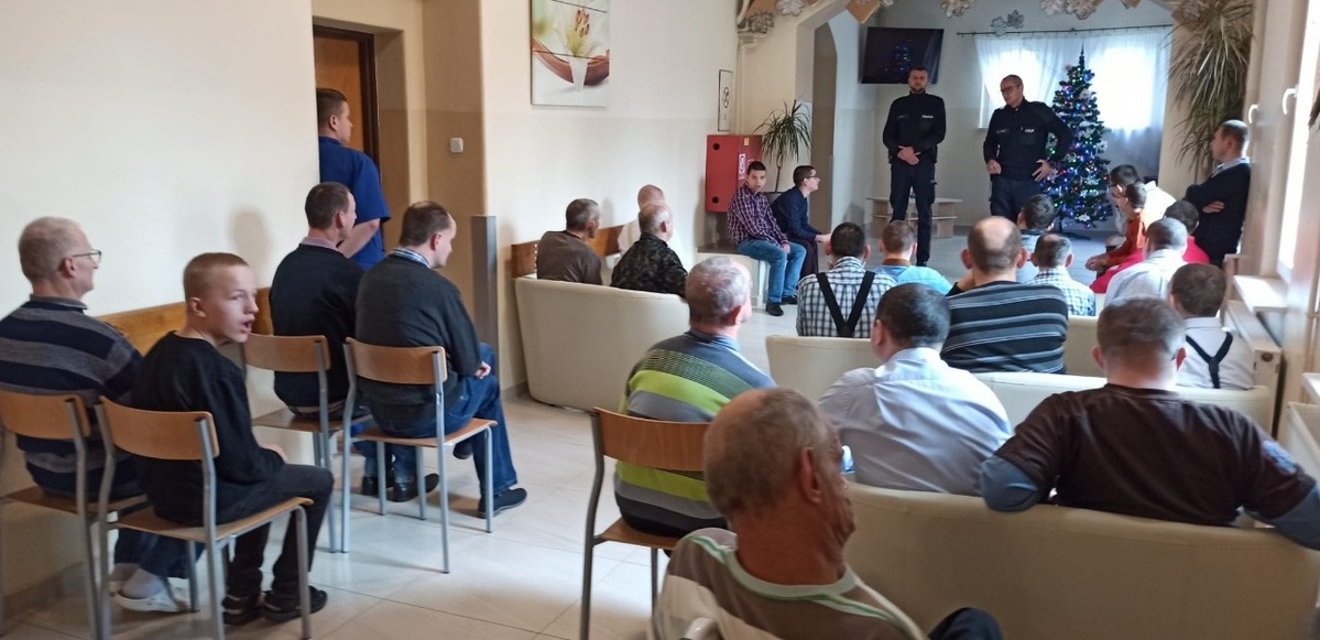 na zdjęciu pensjonariusze słuchają prelekcji policjantów, którzy stoją naprzeciwko nich