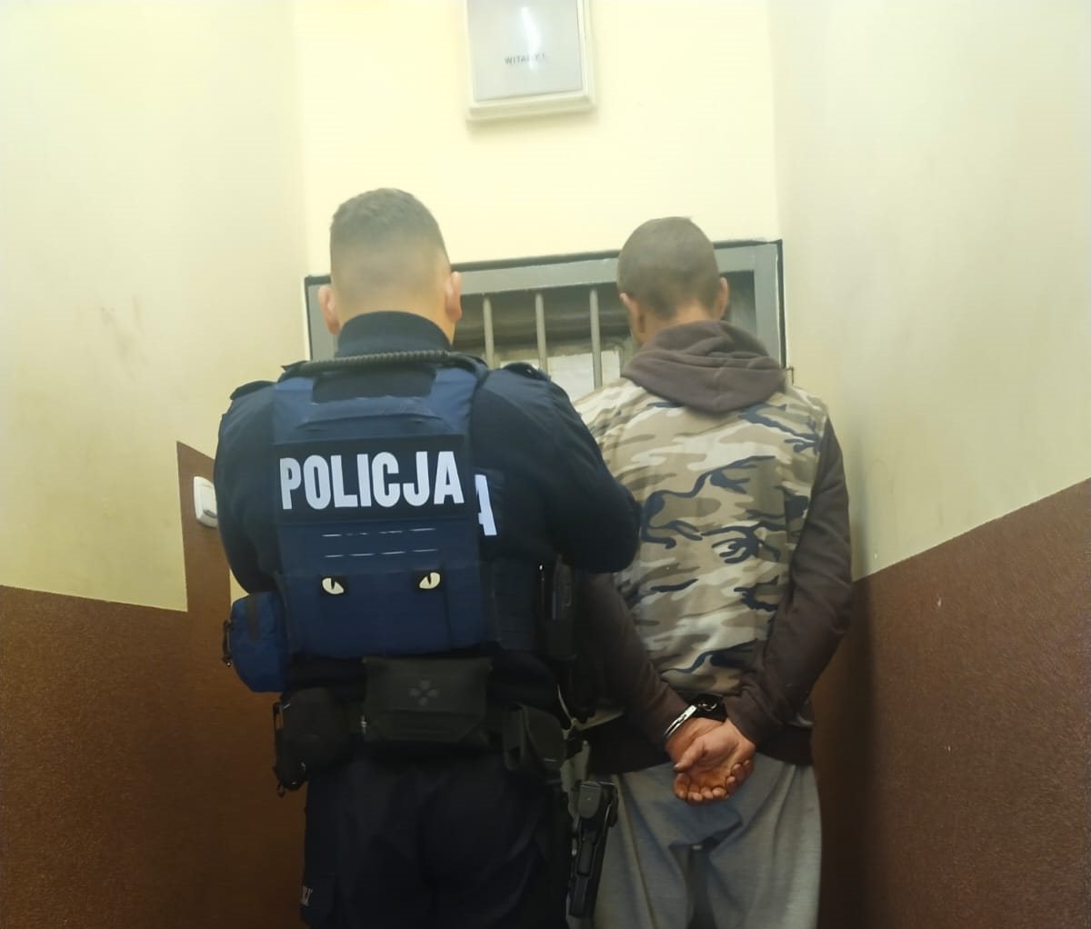 na zdjęciu policjant z zatrzymanym na klatce schodowej