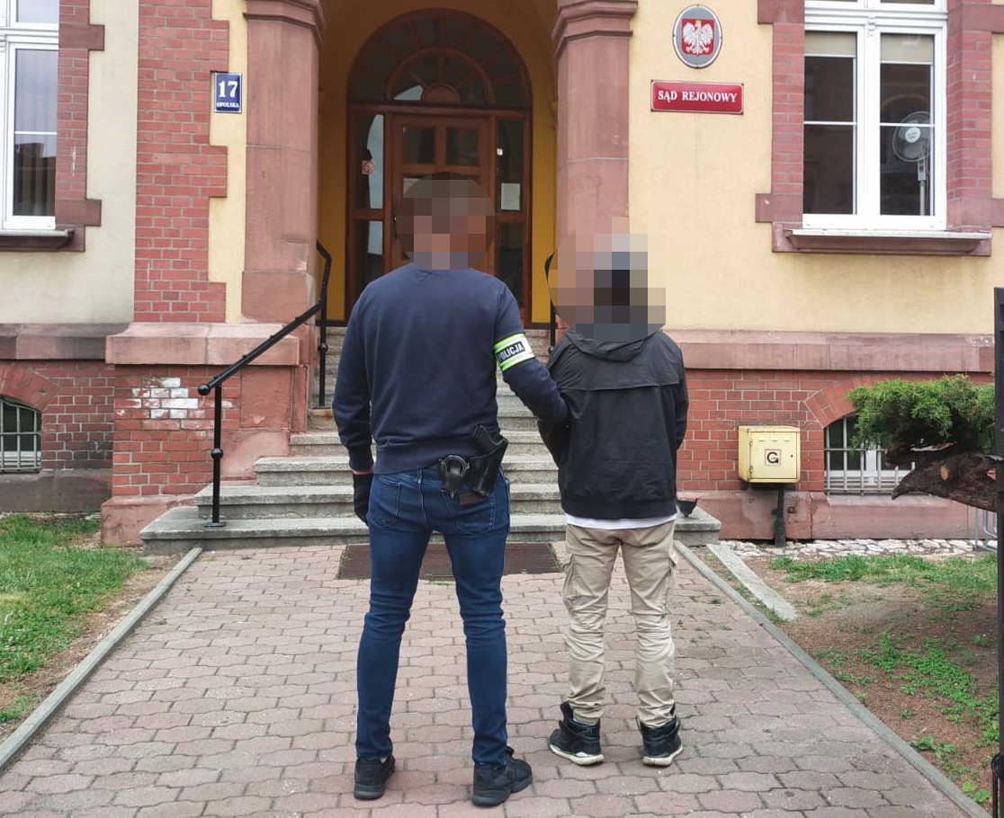 na zdjęciu policjant z opaską na ręku prowadzi zatrzymanego do budynku sądu rejonowego 