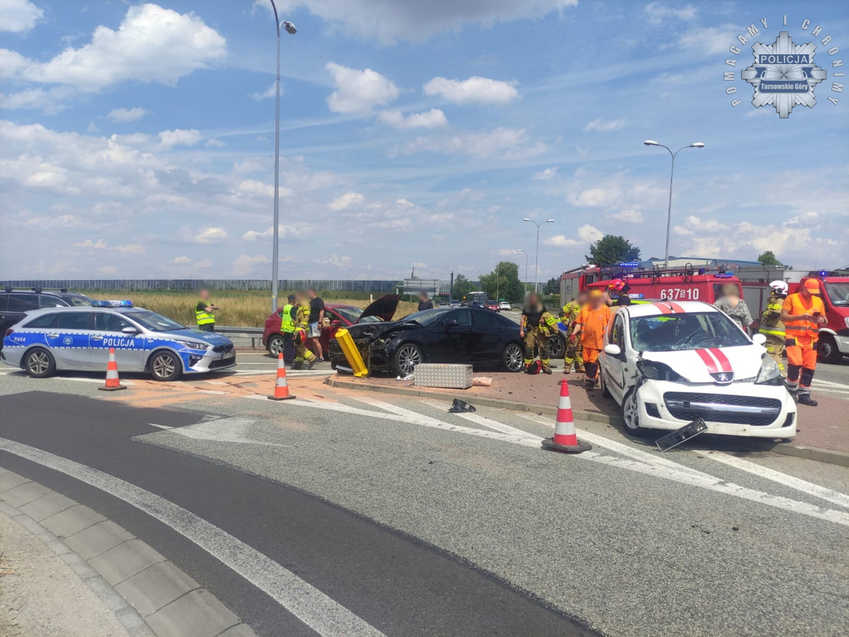 na zdjęciu miejsce kolizji gdzie stoją rozbite auta, obok strażacy policjanci inne osoby i radiowóz i wozy strażackie