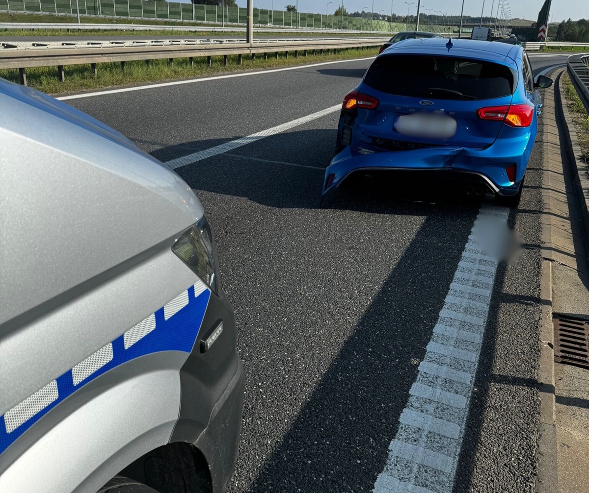na zdjęciu fragment radiowozu na jezdni a przed nim niebieski samochód osobowy z uszkodzonym przodem 