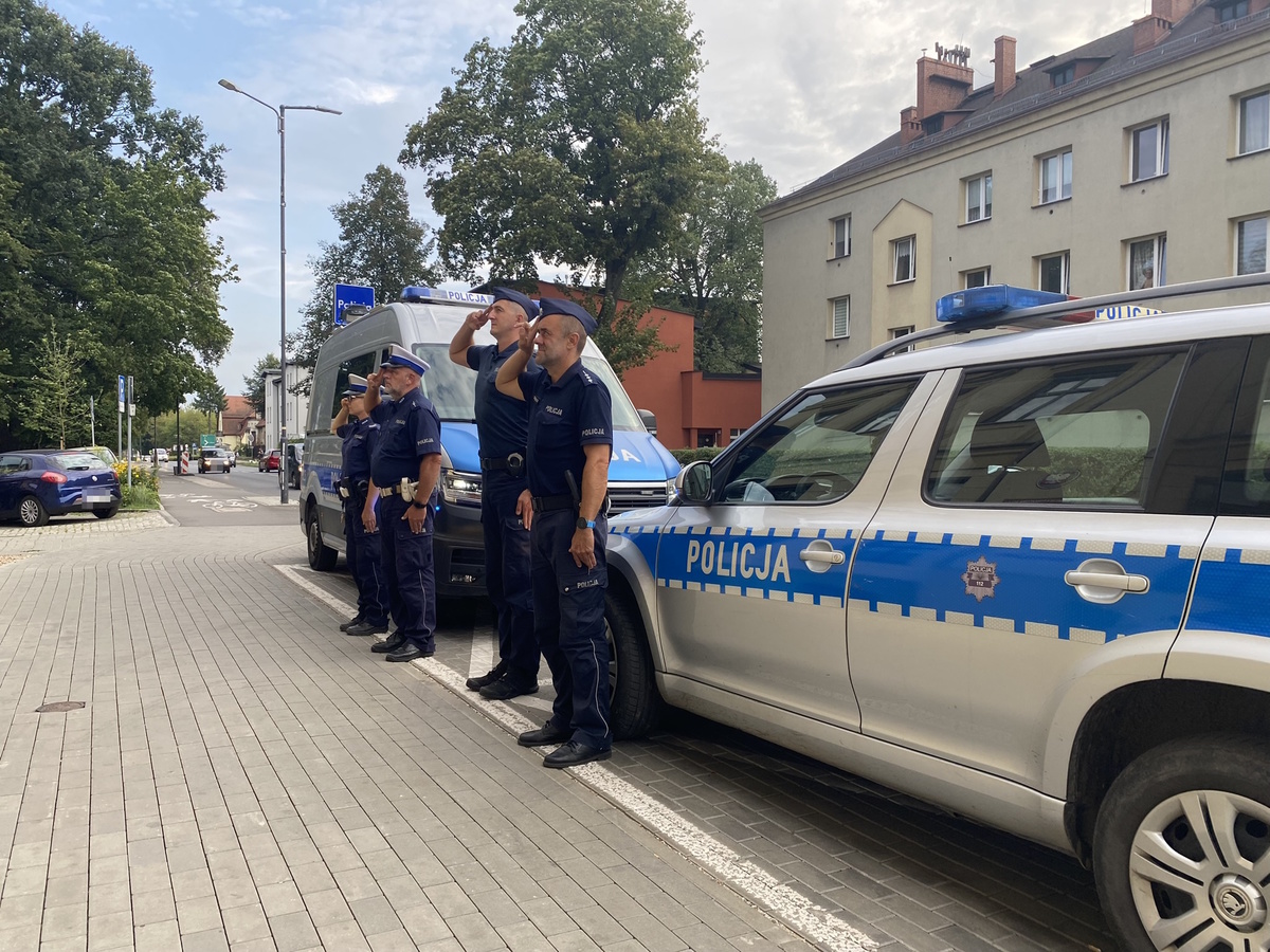 na zdjęciu policjanci przy radiowozach przed komendą, oddający hołd zmarłym strażakom 