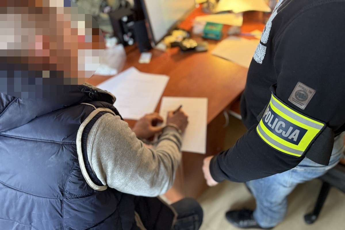 na zdjęciu zatrzymany przy biurku, obok policjant 