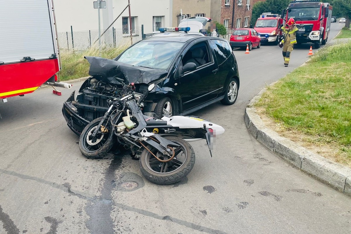 na zdjęciu rozbity samochód i leżący przy nim motorower, za nimi radiowóz i osoby, obok fragment wozu strażackiego