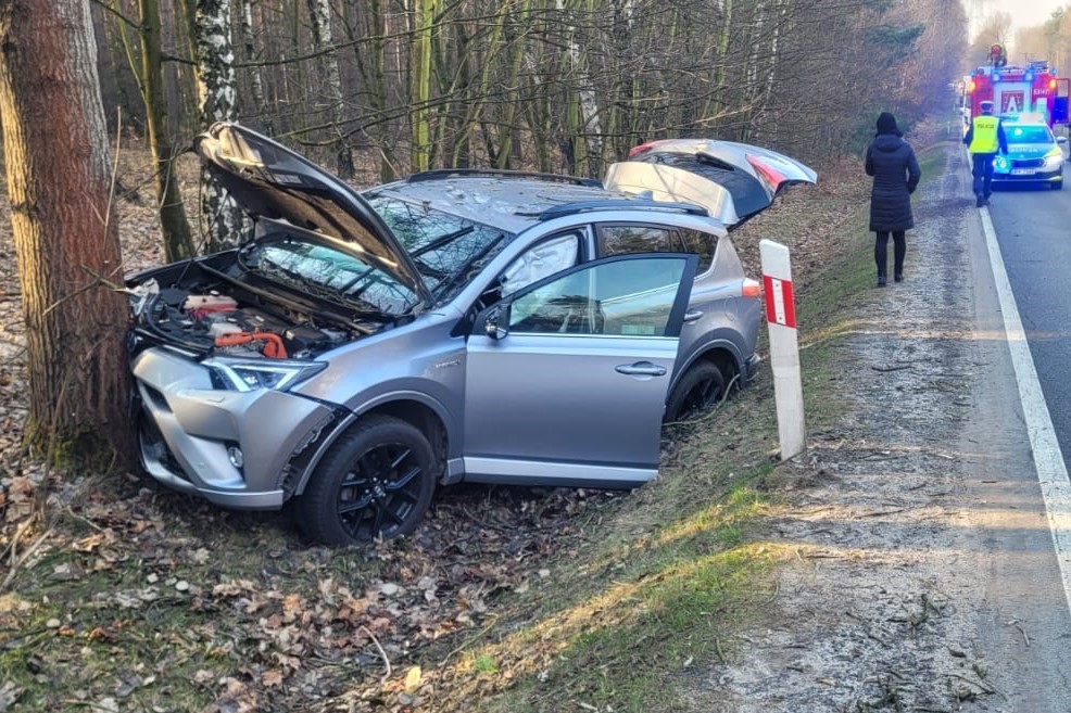 na zdjęciu rozbity samochód przy drzewie, za nim radiowóz i wóz strażacki