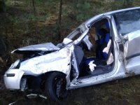 Zdjęcie przedstawia rozbity samochód osobowy. Auto ma wyrwane drzwi od kierowcy