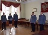 fotografia kolorowa, przedstawiająca komendanta powiatowego w Tarnowskich Górach w towarzystwie zastępcy naczelnika prewencji i specjalisty ds. kadr. Obok nich stoją Odchodzący komendant i przejmujący stanowisko komendanta. W tle godło.