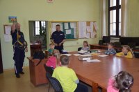 Zdjęcie przedstawia dwóch policjantów i grupę dzieci. Policjant z lewej trzyma w dłoni i prezentuje dzieciom urządzenie pomiarowe wykorzystywane w ruchu drogowym.