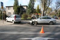 Zdjęcie przedstawia dwa rozbite w wyniku wypadku drogowego samochody. W tle widać inne pojazdy oraz strażaków