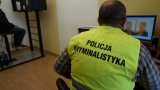 Zdjęcie przedstawia siedzącego tyłem policjanta. Ubrany jest w kamizelkę odblaskową z napisem Policja Kryminalistyka. Wykonuje zdjęcie osobie podejrzanej.