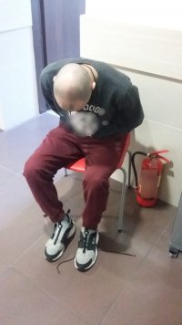 Zdjęcie przedstawia siedzącego na krześle mężczyznę, który został zatrzymany przez policjantów
