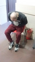 Zdjęcie przedstawia siedzącego na krześle mężczyznę, który został zatrzymany przez policjantów