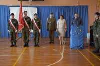zdjęcie przedstawiające przemawiającego Komendanta Policji, dyrektor szkoły, przedstawiciela wojska oraz trzymających sztandar, uczniów szkoły.