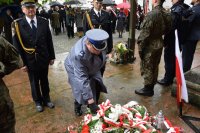 Zdjęcie przedstawia  Pierwszego Zastępcę Komendanta Powiatowego Policji w Tarnowskich Górach podinsp. Sławomira Bylickiego, który pod tablicą składa kwiaty. Obok niego z lewej strony znajduje się  Komendant Straży Miejskiej, a z prawej przedstawiciel Straży Pożarnej.