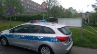Zdjęcie przedstawia radiowóz policyjny z włączonymi sygnałami świetlnymi. Radiowóz zaparkowany jest w miejscu zabezpieczenia niewybuchu.