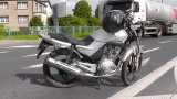 zdjęcie przedstawia zaparkowany na drodze uszkodzony motocykl. W tle widać samochód ciężarowy.