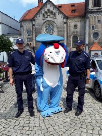 Zdjęcie przedstawia  maskotkę śląskiej policji psa &quot;Sznupka&quot;. Obok maskotki stoją dwaj umundurowani policjanci.