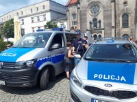 Zdjęcie przedstawia dwa policyjne radiowozy. Pomiędzy nimi stoi policjant oraz odwrócony tyłem chłopiec.
