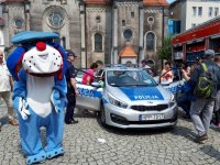 Na zdjęciu (patrząc od lewej strony) widać  maskotkę śląskiej policji psa &quot;Sznupka&quot;, z prawej strony fotografii widać  policyjny radiowóz, do którego wsiadają dorosłe osoby.