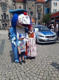 Na zdjęciu (patrząc od lewej strony) widać  maskotkę śląskiej policji psa &quot;Sznupka&quot;, przy którym stoją: chłopiec i dziewczynka. Z prawej strony fotografii widać  policyjny radiowóz.