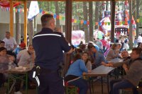Na zdjęciu widać  policjanta asp. szt. Adama Cichowskiego. W tle fotografii widać  grupę siedzących przy stołach osób.
