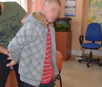 Na zdjęciu widać mężczyznę. Ma założone kajdanki na ręce trzymane z tyłu.