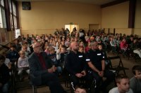 Na zdjęciu widać siedzących na krzesłach dzielnicowych sierż. szt. Grzegorza Szeligę,  st. sierż. Przemysława Lebek, nauczycieli  oraz grupę dzieci ze Szkoły Podstawowej nr 1 w Radzionkowie.