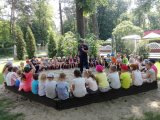 dzielnicowy podczas spotkania z przedszkolakami przemawia przez mikrofon, dookoła niego znajdują się dzieci