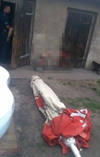 na zdjęciu widać złożony, leżący na ziemi parasol ogrodowy. W tle fotografii widać drzwi do pomieszczeń gospodarczych oraz stojącego w nich policjanta