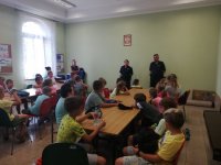 na zdjęciu widać grupę dzieci siedzących przy stołach. W tle widać policjantów