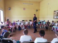 na zdjęciu widać grupę siedzących na krzesłach dzieci. Pośrodku nich znajduję się policjant