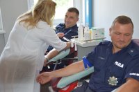 na zdjęciu widać siedzących na fotelach policjantów. Obok nich znajduje się pielęgniarka, która przygotowuje mundurowych do pobrania krwi