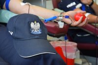 Na zdjęciu widać policyjną czapkę. W tle fotografii widać rękę, z której pobierana jest krew