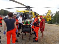 Na fotografii widać helikopter LPR,  policjanta, grupę ratowników medycznych i WOPR. Widać również nosze, na których leży poszkodowany mężczyzna