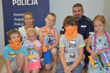 Na fotografii widać policjanta, nauczyciela oraz grupę dzieci. W tle fotografii widać policyjny baner