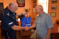 Na fotografii widać inspektora Krzysztofa Hajdę oraz Pana Mirosława. Komendant dziękuje mu za pomoc i wręcza drobne upominki z logo kampanii &quot;Nie reagujesz -  akceptujesz&quot;.