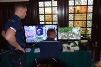 Na fotografii widać dwóch policjantów obserwujących monitory, na których widać uczestników imprezy.