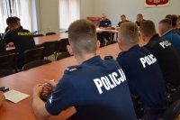 Na fotografii widać salę odpraw, na której przy stole siedzą policjanci.