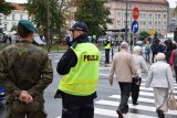 Na fotografii widać stojących przy przejściu dla pieszych policjanta oraz wojskowego. Z prawej strony zdjęcia widać ludzi przemieszczających się przez przejście dla pieszych.