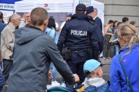 Na fotografii widać ludzi. Pośród nich widać odwróconego tyłem policjanta.